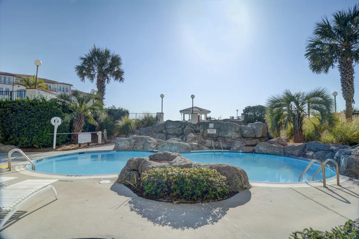 A beautifully landscaped pool area features unique rock formations, palm trees, a cabana, and plenty of lounge chairs for basking in the sun. The setting is lively yet peaceful, perfect for poolside socializing or quiet mornings by the water.
