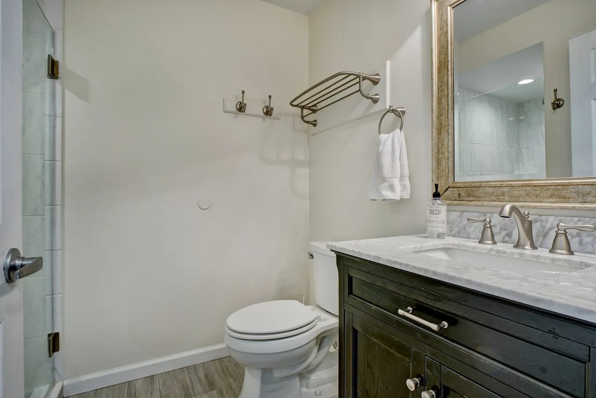 A serene bathroom scene displaying a vanity with a marble countertop, a large mirror, a modern shower stall, and toilet. The space feels refreshing and tranquil, perfect for relaxing self-care routines after a day at the beach or pool.