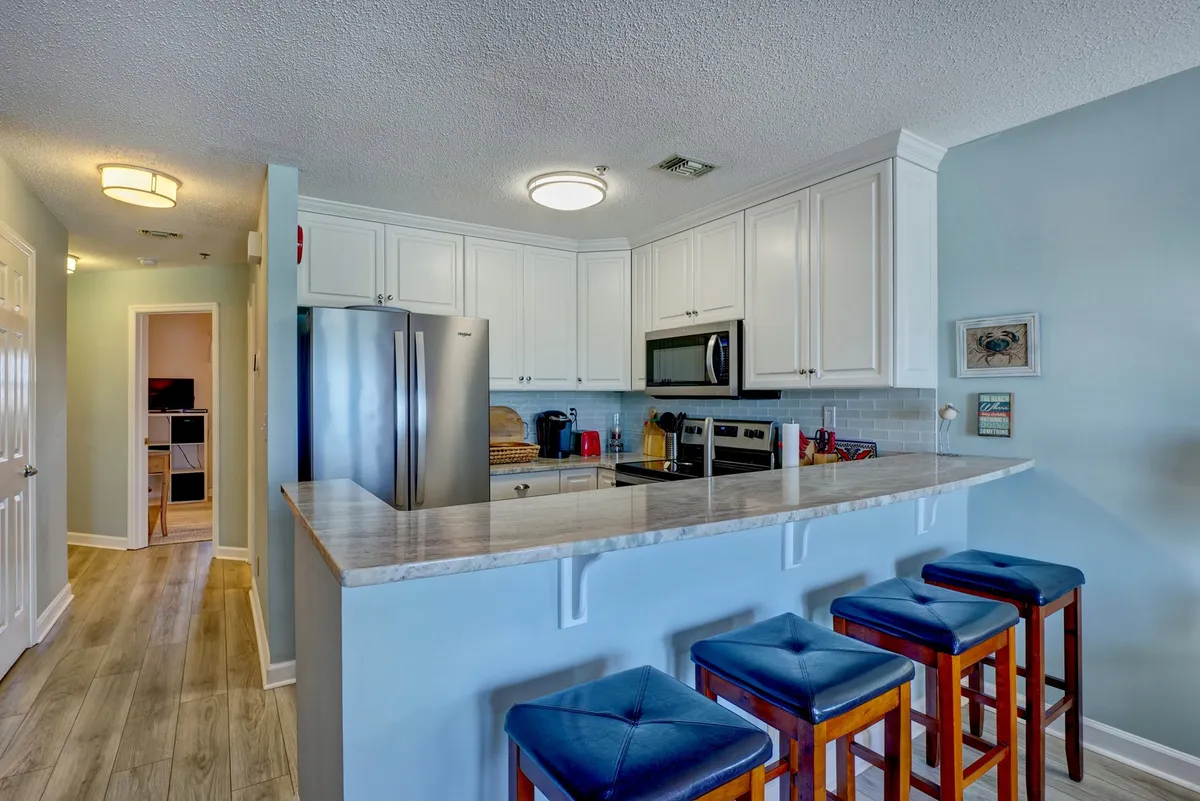 A modern, fully equipped kitchen featuring a kitchen island with bar stools, gleaming stainless steel appliances, and crisp white cabinetry. The setup is ideal for both casual family breakfasts and more elaborate meal preparations, with a functional, inviting atmosphere.